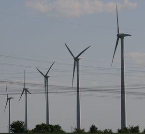 Low angle view of wind turbines on field against sky