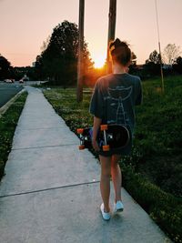 Woman with skateboard walking on footpath during sunset