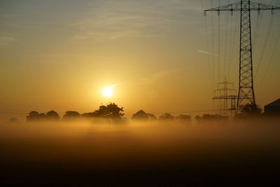 Silhouette electricity pylon against sky during sunset