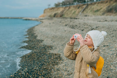 A little girl squinting photographs the autumn seascape on a childrens pink camera. the child is