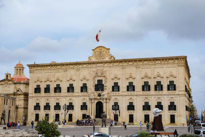 Group of people in front of historical building against cloudy sky