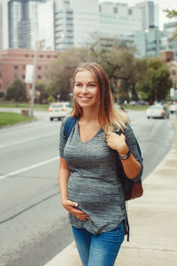 Portrait of smiling young woman standing on road in city