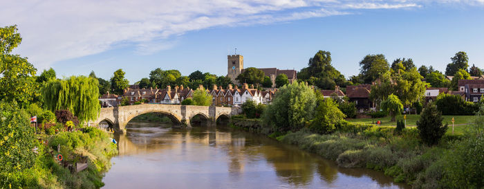 Bridge over river by buildings against sky