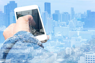 Digital composite image of hands holding smart phone against cityscape