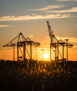 Silhouette cranes at construction site against sky during sunset