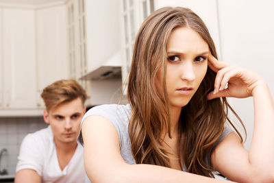 Portrait of serious woman sitting by boyfriend at home