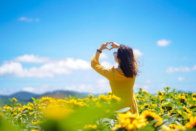 Low angle view of woman standing on yellow flowering plant against sky