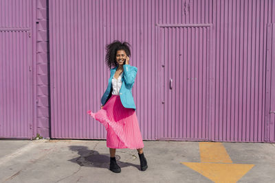 Full length portrait of woman standing against pink wall