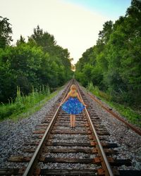 Rear view of woman standing on railway tracks amidst trees