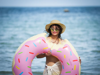 Portrait of woman holding donut pattern inflatable ring at beach