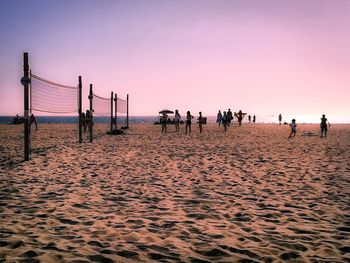 People at beach against clear sky during sunset