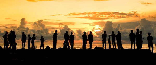 Silhouette people on beach against sky during sunset