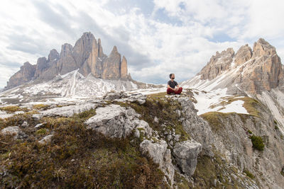 Distant view of hiker sitting on rough rock and admiring view of dolomites mountains in winter