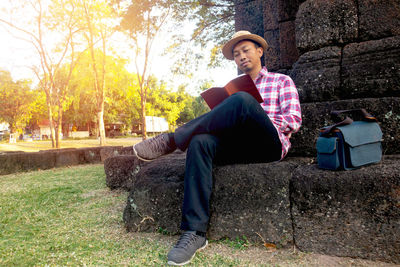 Full length of young man reading book while sitting on land