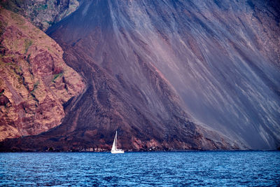 Distant view of sailboat on sea against mountain