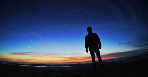 Silhouette of man standing on beach at sunset