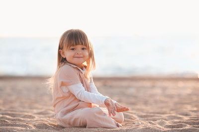 Portrait of cute girl sitting on sand at beach