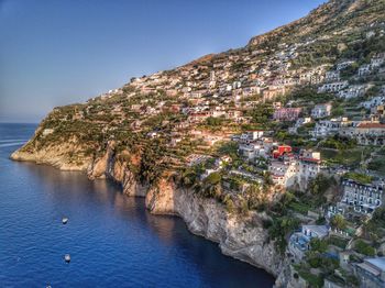 Scenic view of sea by mountains against clear blue sky