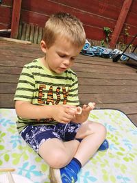 Boy playing with snack while sitting on picnic blanket at hardwood floor