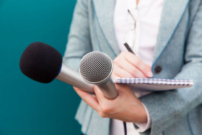 Close-up of woman holding microphone and note pad against colored background