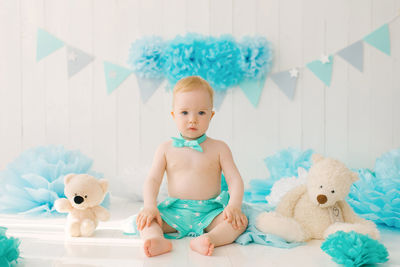 A baby is sitting next to soft teddy bears in a festive birthday decor, a one-year-old boy in blue 