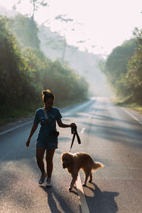 Rear view of woman with dog walking on road