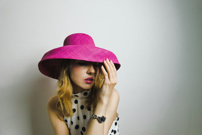 Young woman wearing pink hat against white wall