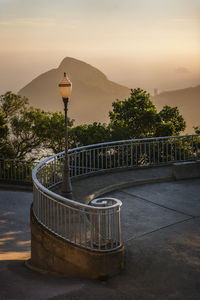 Old street lamp in rio de janeiro,  spiral curved iron handrail, trees,  sugar loaf mountain at dusk