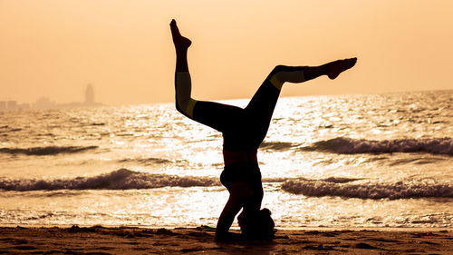 Full length of silhouette man climbing on beach against sky during sunset