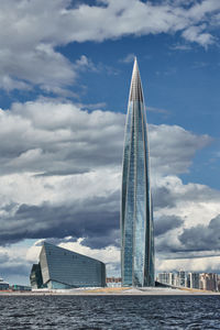 Modern buildings by river against cloudy sky