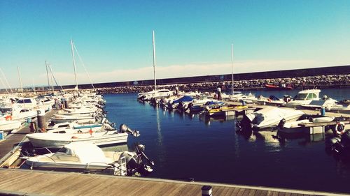 Boats moored at harbor against clear blue sky