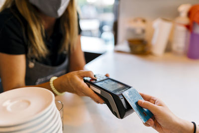 Female cashier receiving payment through credit card from customer in cafe during covid-19