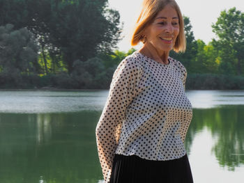 Portrait of young woman standing against lake