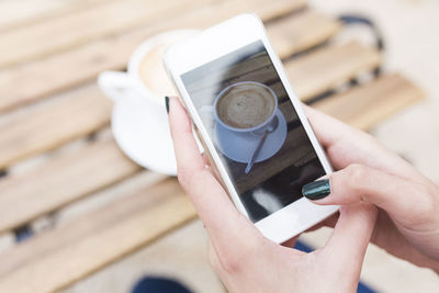 Woman taking a photo of her cappuccino with smartphone, close-up