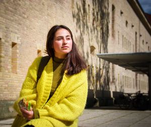 Beautiful woman sitting by building in city