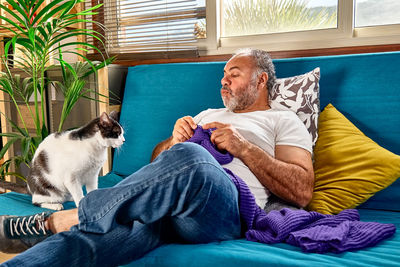 Bearded man plays with his cat while knitting as part of his hobby to keep a positive mental health
