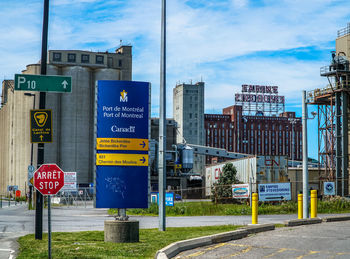 Road sign by buildings against sky in city