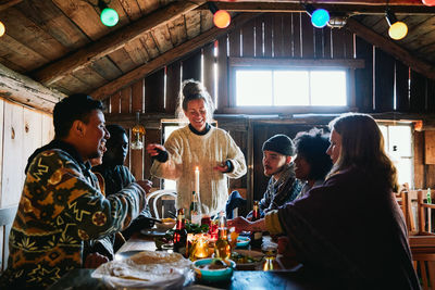 Smiling young woman talking while enjoying meal with friends in cottage