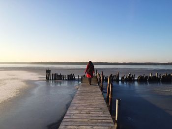 Rear view of woman on pier at beach against clear sky