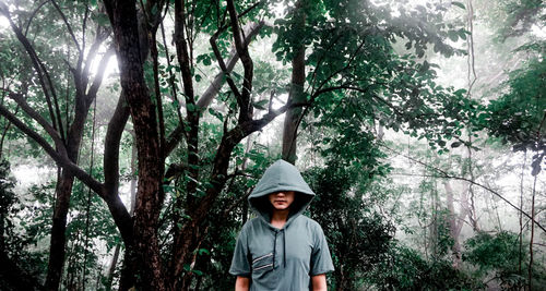 Man with hooded shirt standing against trees in forest