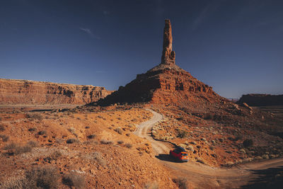 An orange car is driving through the valley of gods, utah