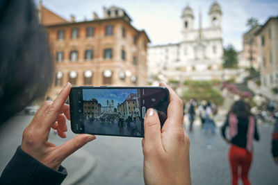 Cropped image of hand holding smart phone in city