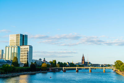 View of buildings by river against blue sky