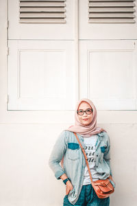 Portrait of smiling young woman standing against wall