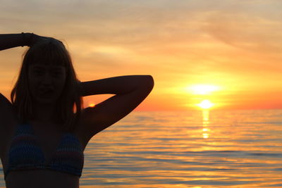 Woman standing by sea against sky during sunset