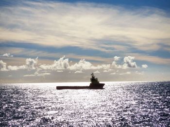 Boat sailing on calm sea against cloudy sky
