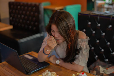 Young woman using phone while sitting on table