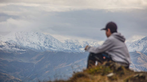 Side view of man sitting on mountain against sky