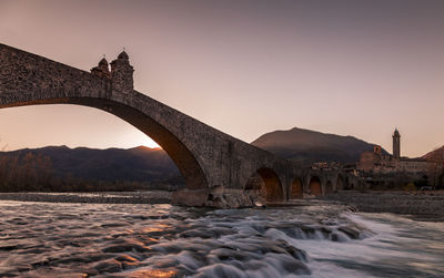 Landscape of a medieval bridge over a turbulent river at sunset in winter