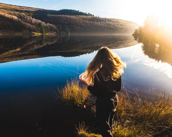Rear view of woman standing by lake against sky